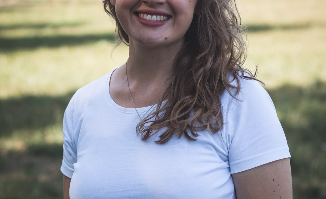 Eine lächelnde Frau in einem weißen T-Shirt steht auf einem Feld.